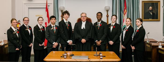 A picture of the student pages in the legislative chamber with Speaker Hon. Colin LaVie.