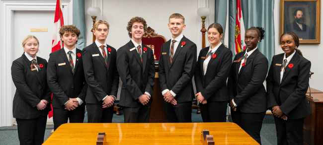 A group photo of 8 of the 9 pages for the 2025-26 school year standing in the legislative chamber.