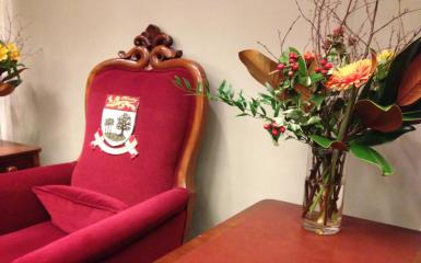 A picture of the Speaker's chair and a vase of flowers on the table beside it.